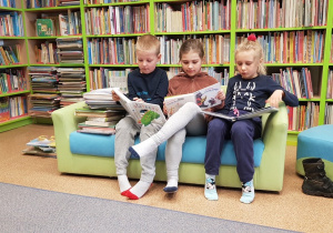 Trójka dzieci na zielonej kanapie czytają książki